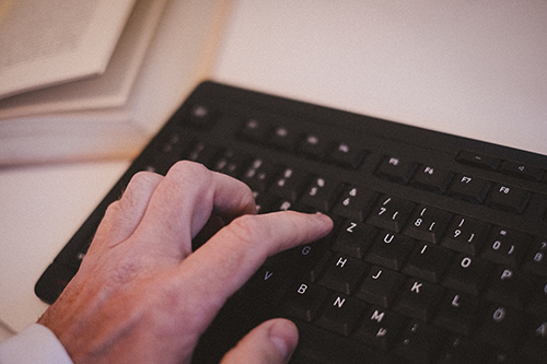 Hand an einer Tastatur und ein Buch im Hintergrund; Bild: Michael Schnell