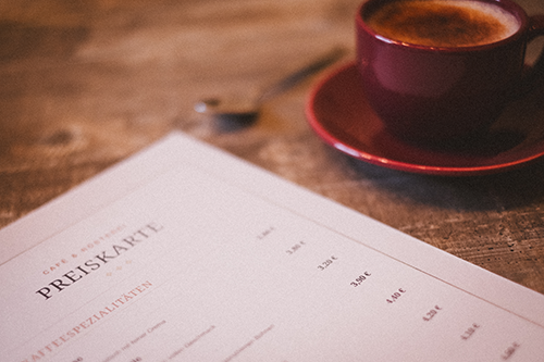 Kaffeetasse und Preiskarte eines Cafés (Preiskarte mit KI erstellt, anschließend ausgedruckt)
